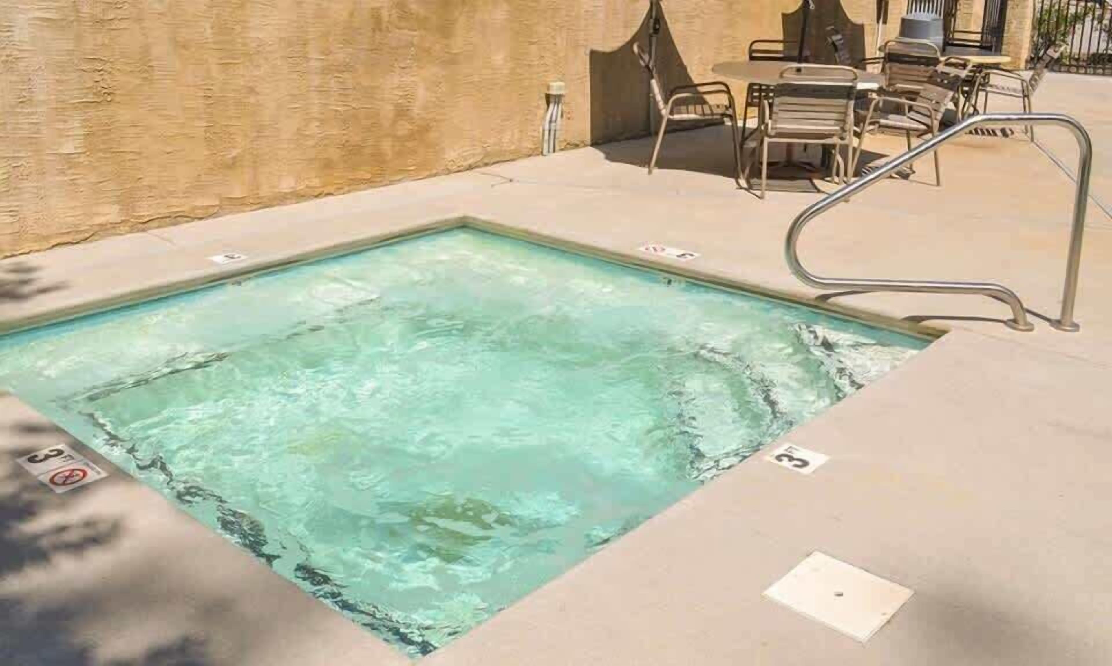 Ein rechteckiger Pool mit klarem Wasser, umgeben von einer Betonplattform und Metallstühlen.