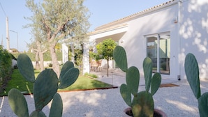 Een binnentuin met terracotta potten en cactussen, een wit gebouw met een betegeld dak, en een gazon met een tafel en stoelen.