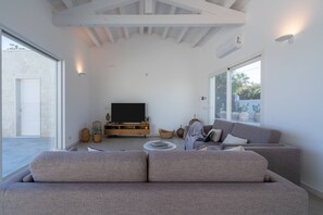 A modern living room with a large grey sofa, a flat-screen TV, and a coffee table. - Charming Villa in Fontane Bianche, Italy - Perfect for Families (Syracuse)