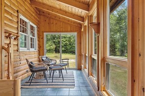 A log cabin with a porch, wicker chairs, and a view of the forest. - Blueberry Cottage on the Ocean! (Lamoine)