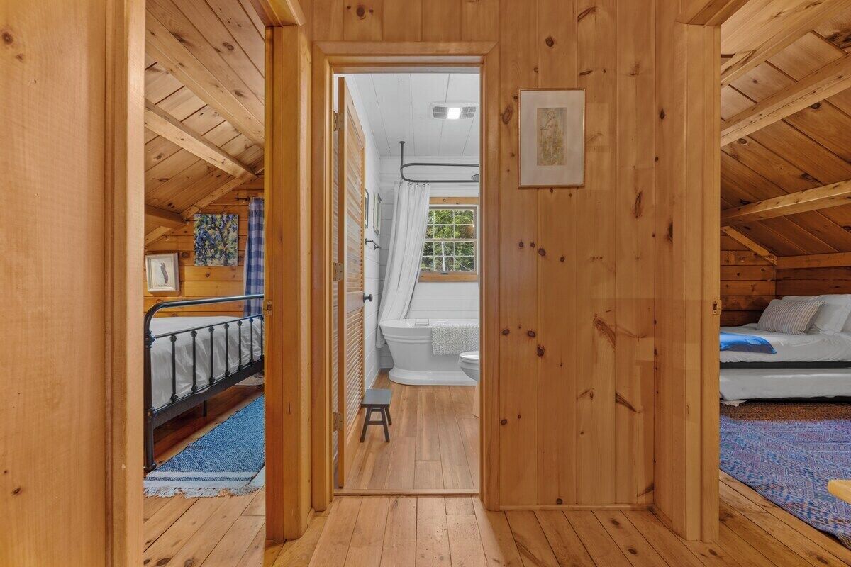 Un interior de madera con una cama litera, un baño con inodoro y ducha, y un taburete pequeño.