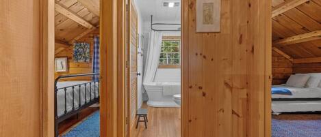 Un interior de madera con una cama litera, un baño con inodoro y ducha, y un taburete pequeño.