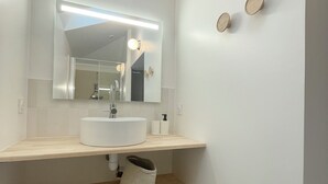 A bathroom with a white sink, a mirror, and a light fixture above it. There are two round wall decorations and a trash can.