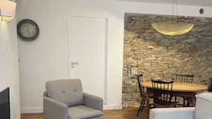 A modern living room with a stone wall, a dining table with chairs, a grey armchair, and a wooden coffee table.