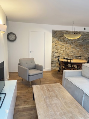 Een moderne woonkamer met een stenen muur, een eettafel met stoelen, een grijze fauteuil en een houten salontafel.