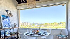 A dining area with a table set for four, white chairs, a hanging light fixture, and a view of a cityscape through a large window.