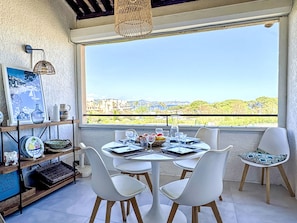 Uma área de refeições com mesa posta para quatro, cadeiras brancas, luminária pendente e vista para o horizonte urbano através de uma janela grande.