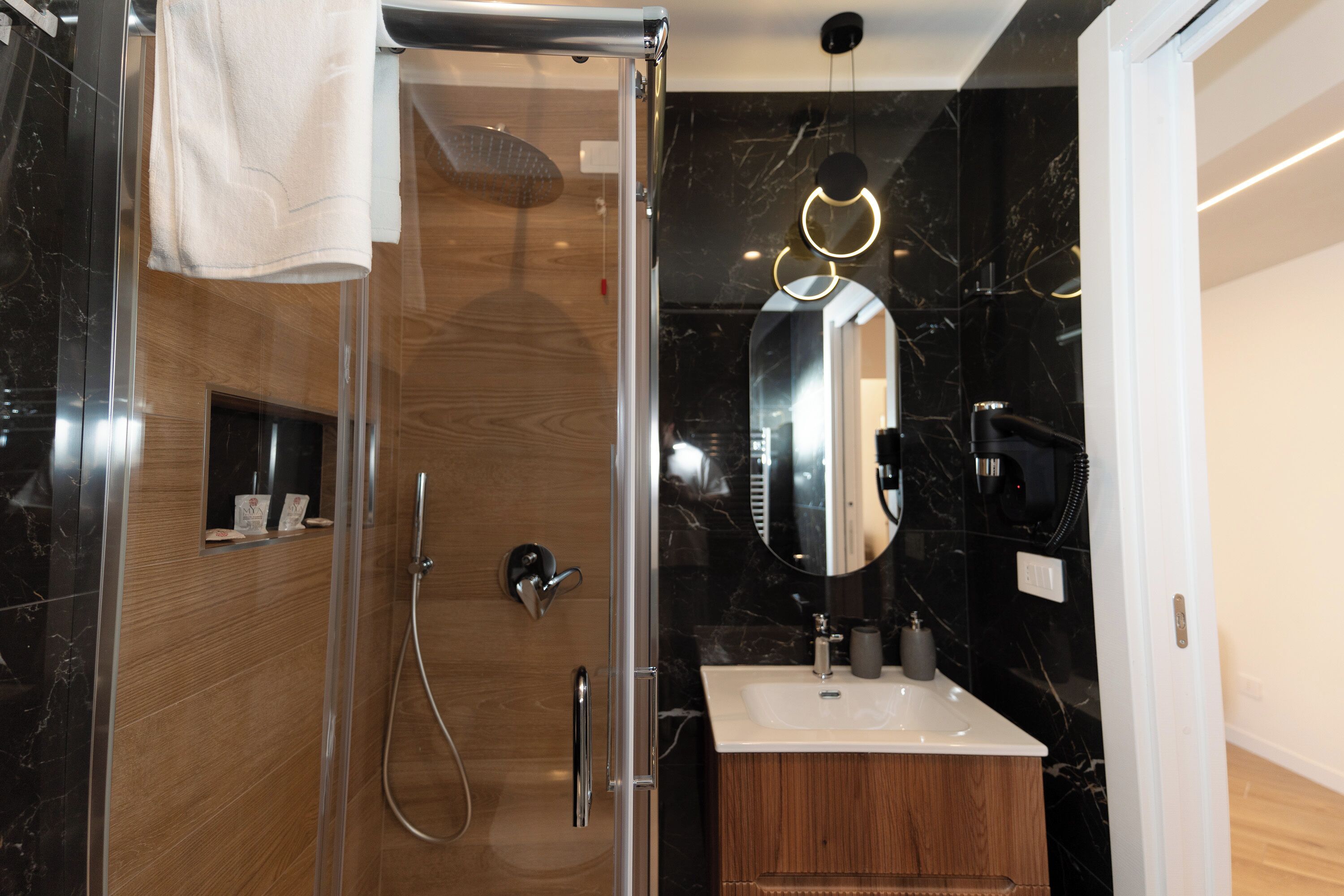 A modern bathroom with a glass-enclosed shower, a wooden vanity, a large mirror, and a marble backsplash.