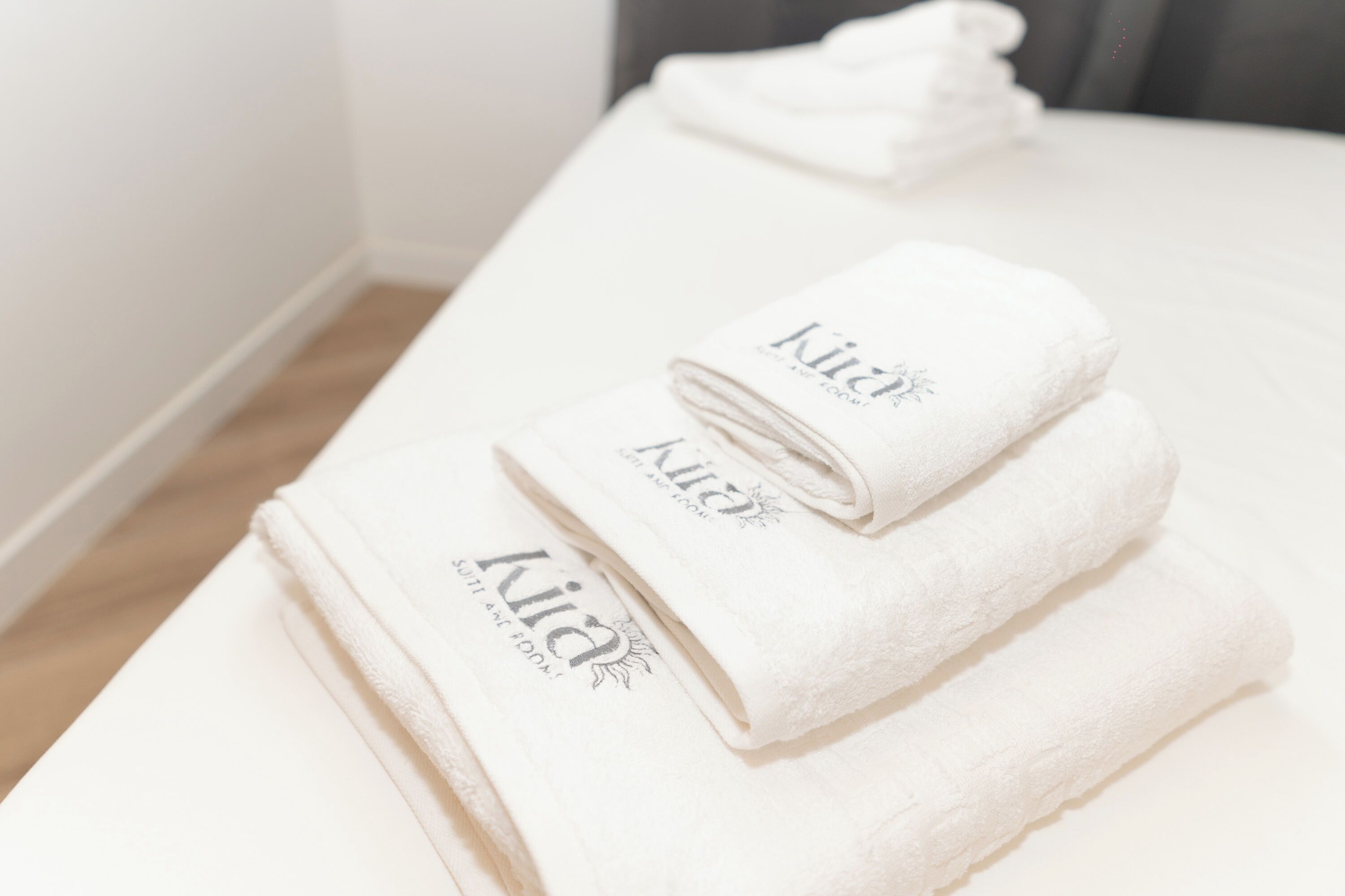 Des serviettes blanches, soigneusement pliées, portant le nom de la marque « Kia », sont posées sur une surface propre et blanche, probablement dans une chambre d’hôtel.