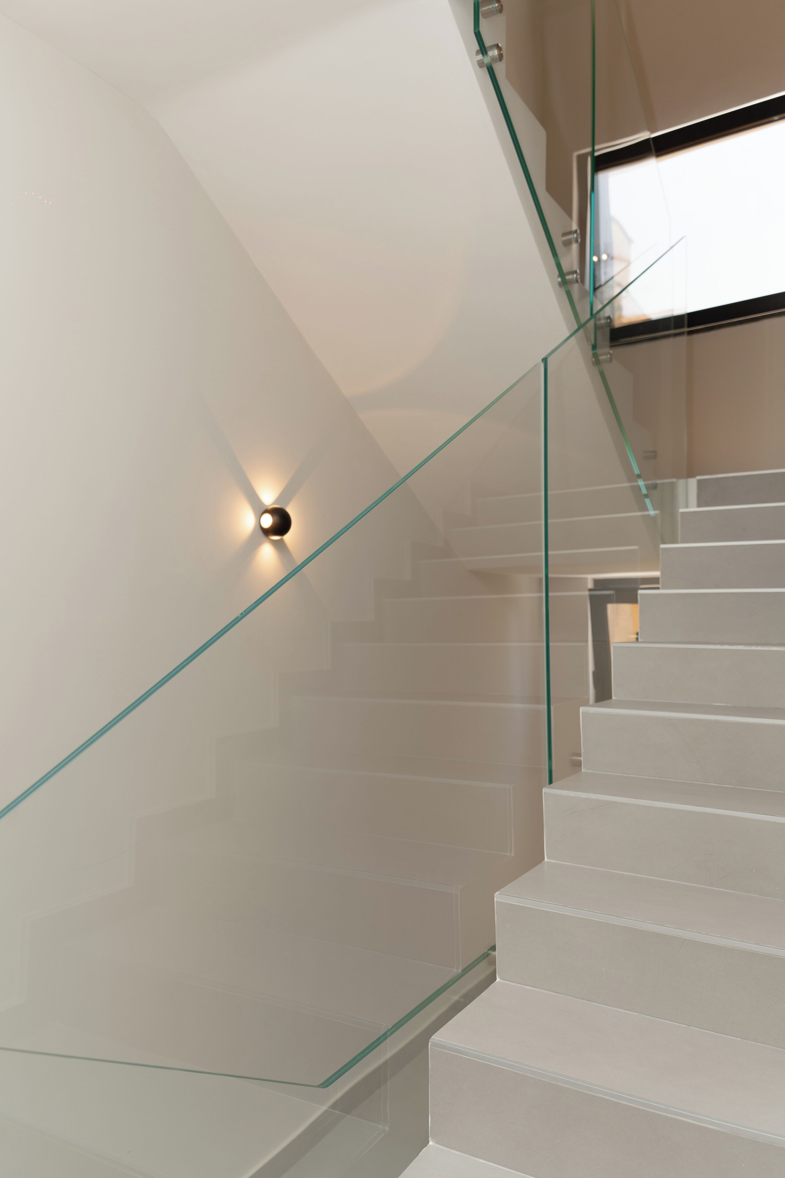 A modern staircase with glass railings and a wall-mounted light fixture.