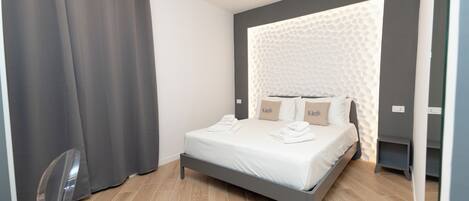 Ein modernes Schlafzimmer mit grauem Bett, weißen Leinen und einer strukturierten Wand dahinter.