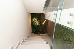 A modern staircase with a glass railing, a neon sign, and a green wall with plants. - Kira Suite and Rooms (Pozzuoli)