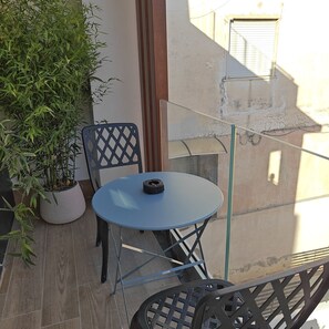A small outdoor balcony with a blue table and chairs, a potted plant, and a view of the building's exterior. - Kira Suite and Rooms (Pozzuoli)