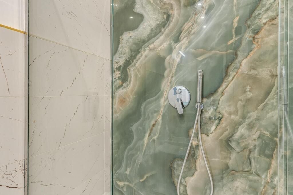 Een badkamer met een marmeren wand en een douche met een handdouche.