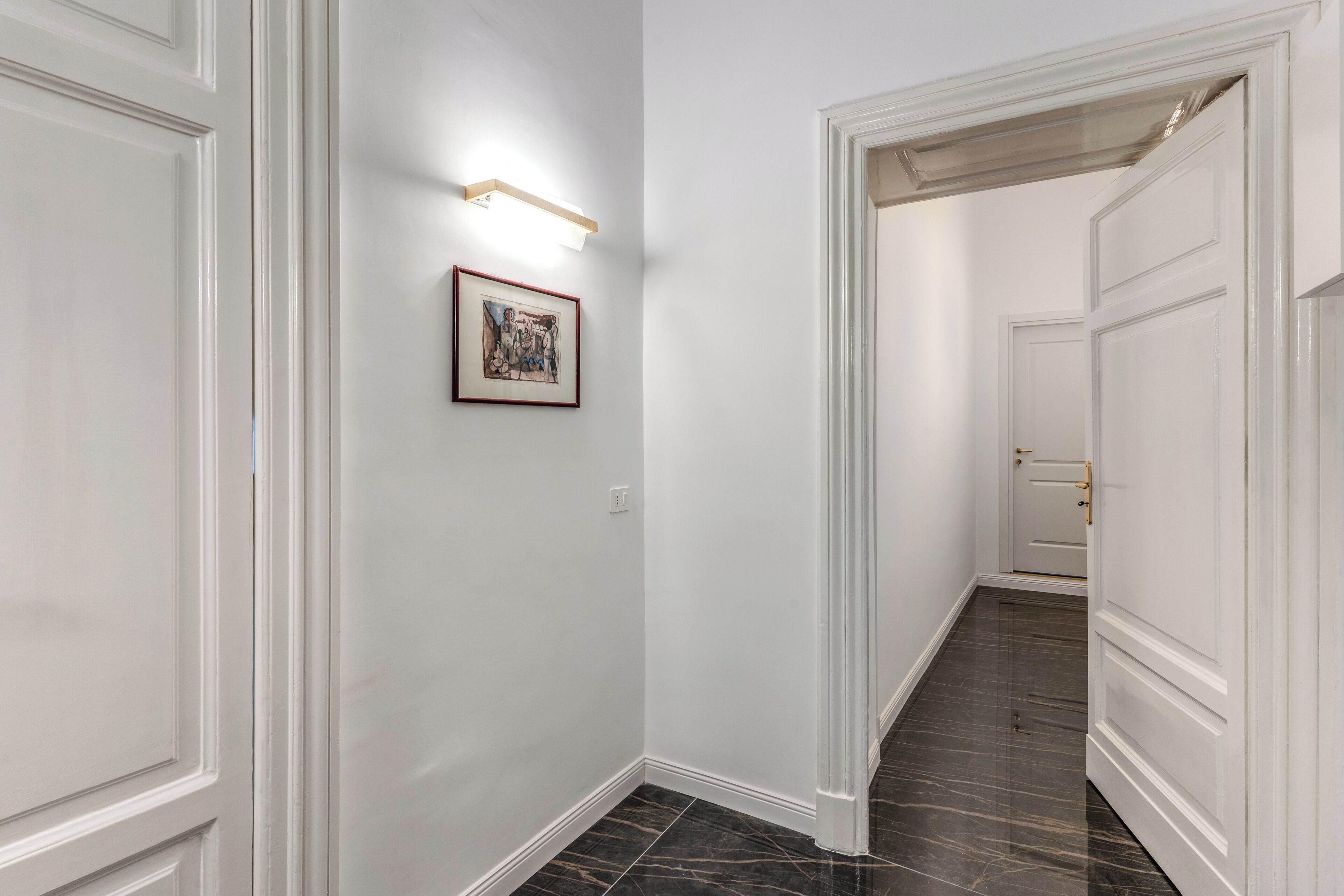 Um corredor com paredes brancas, um quadro emoldurado e um luminário.
