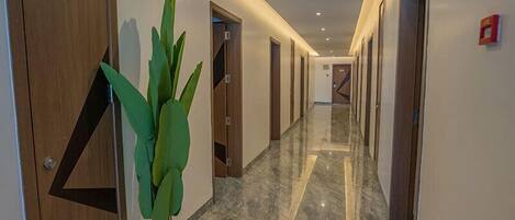 A hallway with wooden doors, a potted plant, and a marble floor.