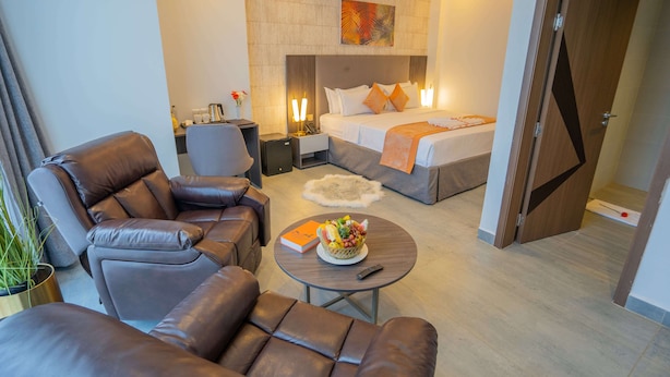 Una habitación de hotel moderna con sofá, sillón y una pequeña mesa redonda con frutero.