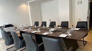 Un salón de conferencias con una larga mesa, sillas negras, botellas de agua y un proyector.