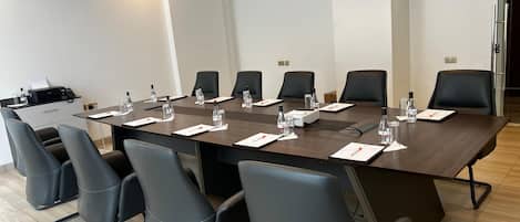 Une salle de conférence avec une longue table, des chaises noires, des bouteilles d’eau et un projecteur.