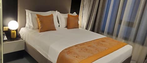 Ein Hotelzimmer mit Bett, Nachttisch mit Lampe und einem Fenster mit Vorhängen.