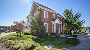 Une maison à deux étages, construite en briques, avec un porche à l’avant et une pelouse bien entretenue.