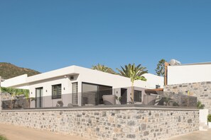 A modern house with a stone wall, large windows, and a balcony. - Mousses Villa, with Pool & Spa Whirlpool by the Beach (CQ4M+QX3 Bali, Greece)