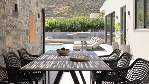 A dining area with a table and chairs, a bowl of fruit, and a glass. - Mousses Villa, with Pool & Spa Whirlpool by the Beach (CQ4M+QX3 Bali, Greece)