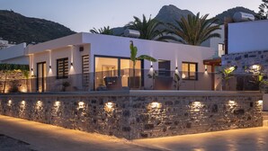 A modern house with a stone wall, large windows, and outdoor lighting. - Mousses Villa, with Pool & Spa Whirlpool by the Beach (CQ4M+QX3 Bali, Greece)