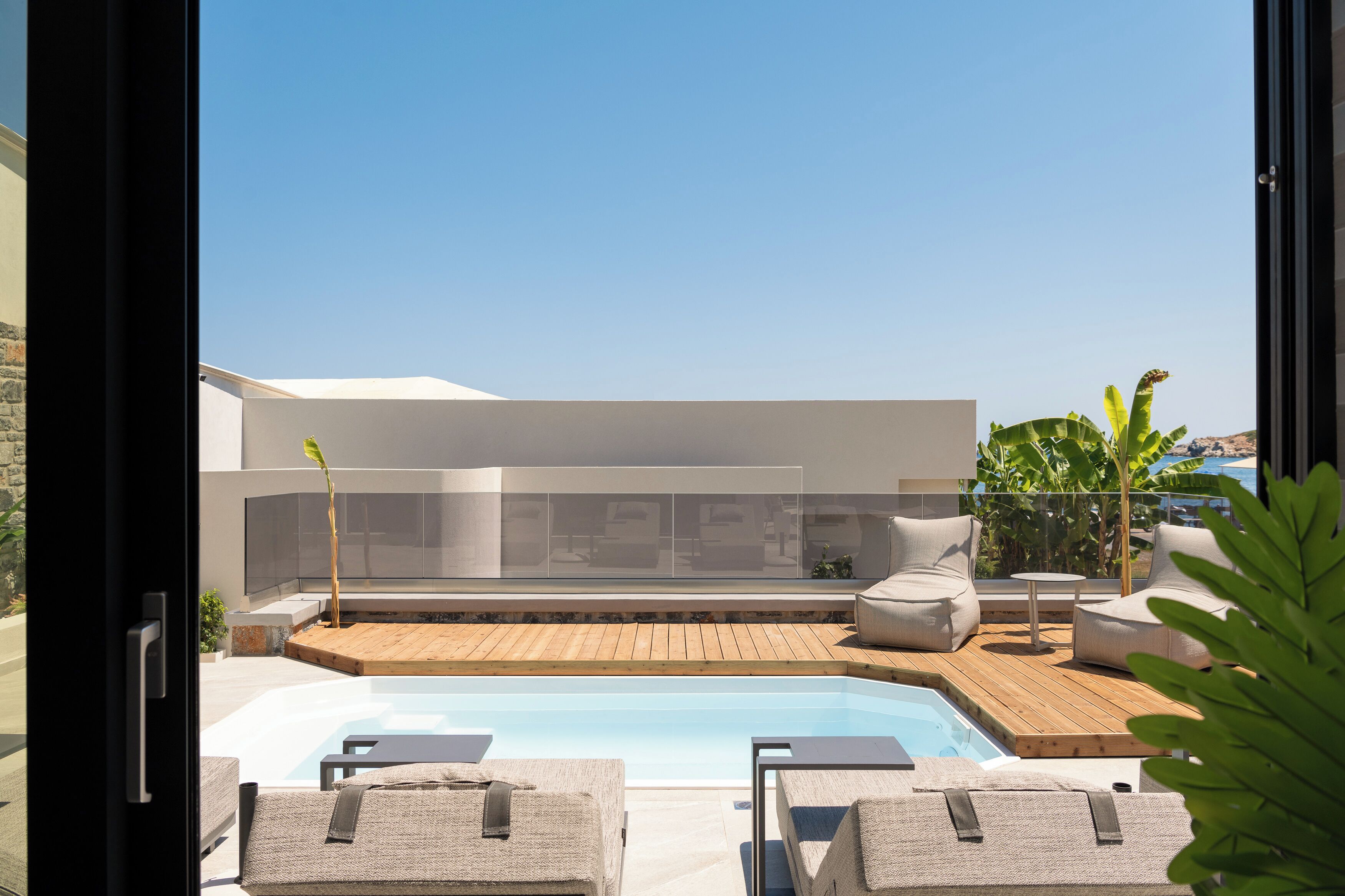 A modern outdoor pool area with lounge chairs, a wooden deck, and a clear view of a building in the background.