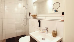 Un baño moderno con un lavamanos blanco, inodoro y zona de ducha con mampara de vidrio.