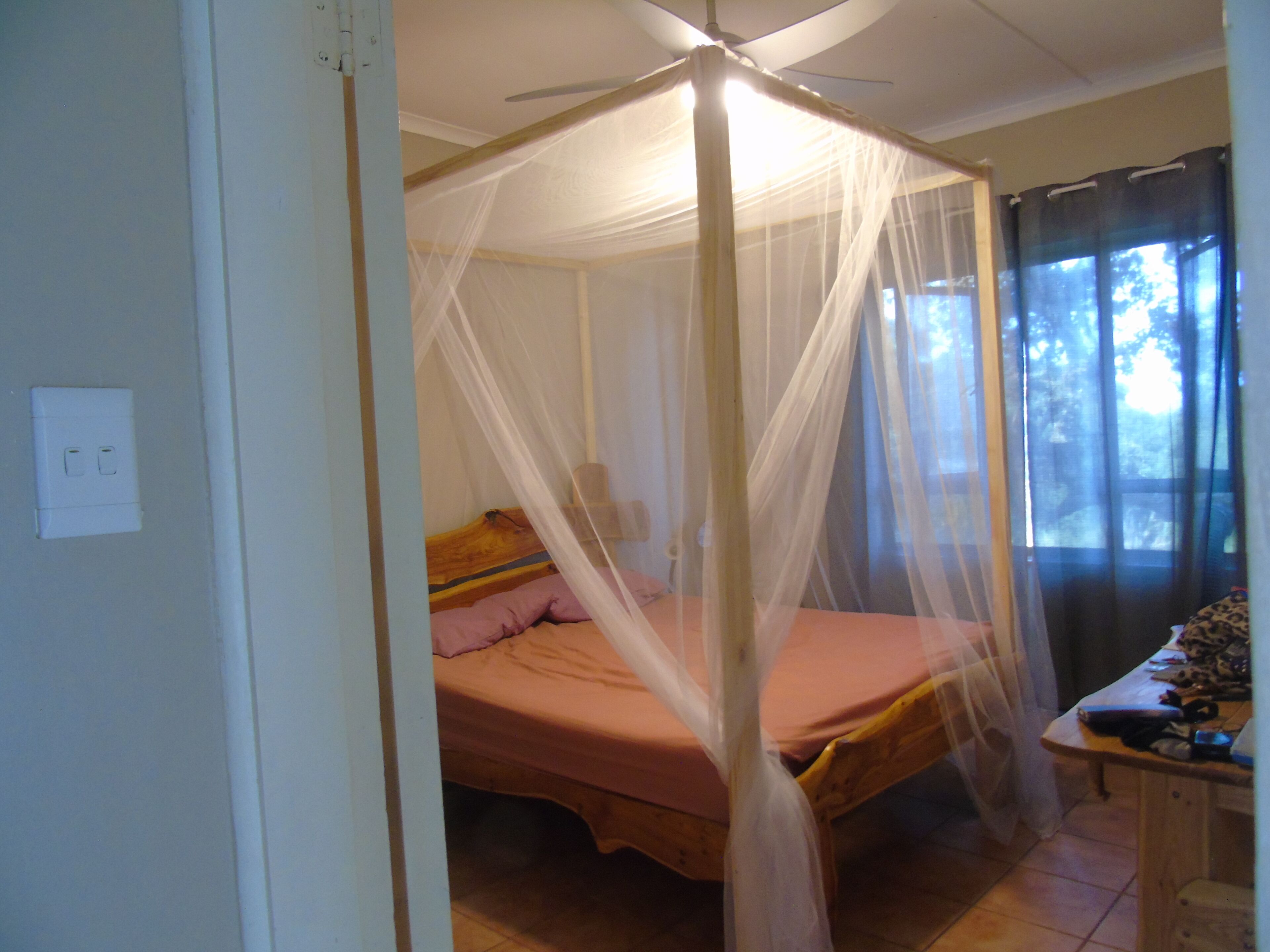 A room with a bed under a canopy, a window with curtains, and a desk with items on it.