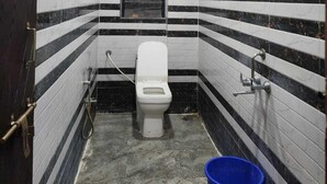 Un baño pequeño y estrecho con azulejos blancos y negros a rayas, un inodoro, un cubo azul y un cabezal de ducha.