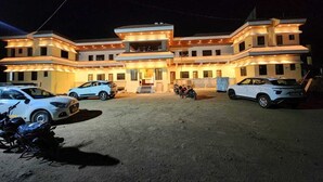 Un edificio de varios pisos con una entrada central y un área cubierta. Varias automóviles y motocicletas estacionadas al frente.
