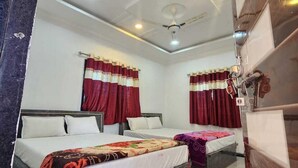 Habitación de hotel con dos camas, cada una con una colcha de estampado diferente, almohadas blancas y cortinas rojas. La habitación tiene un techo blanco con iluminación empotrada y un ventilador de techo.