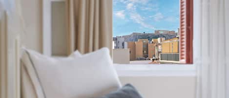 A hotel room with a bed, a window with curtains, and a view of a cityscape with buildings and a hill.