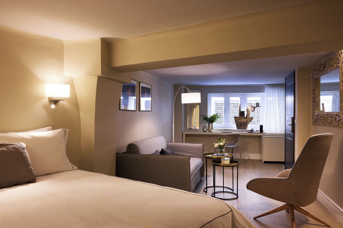 A hotel room with a bed, a sofa, a chair, a small table, and a window with a view.