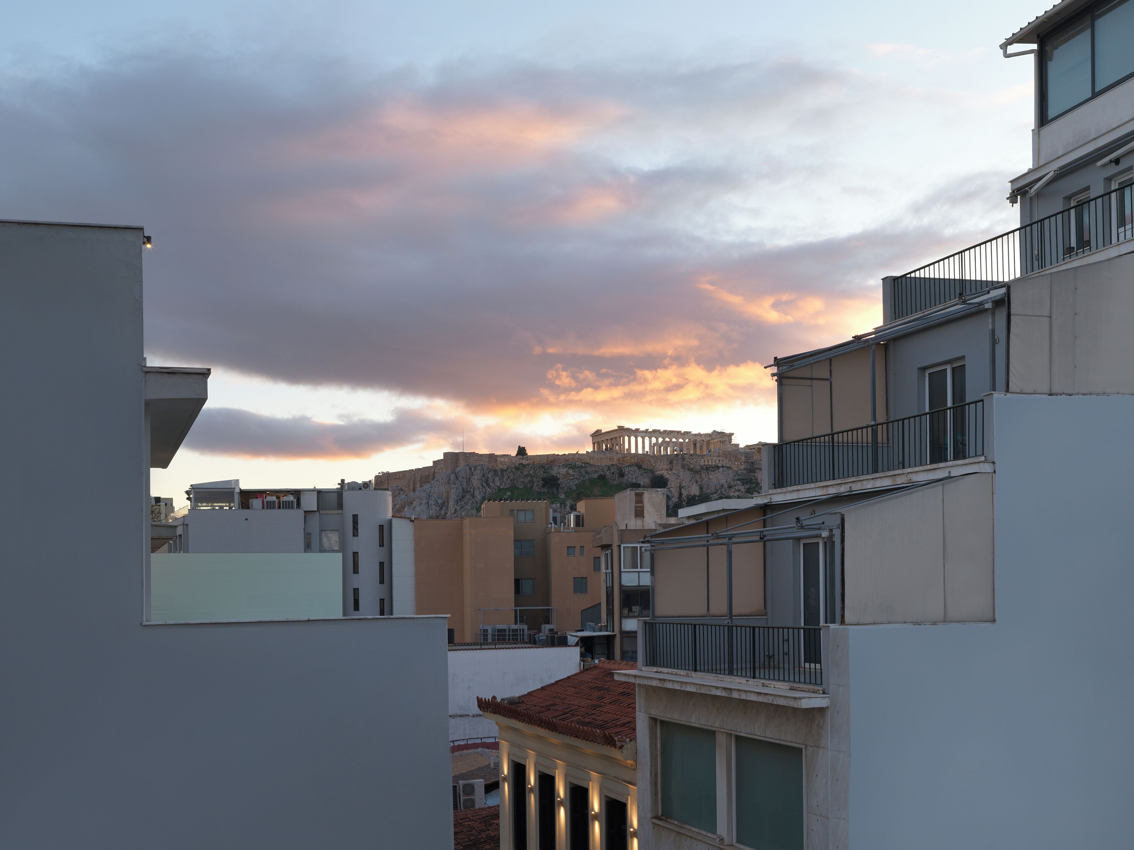 A view of a modern building with balconies and a classical structure in the background.