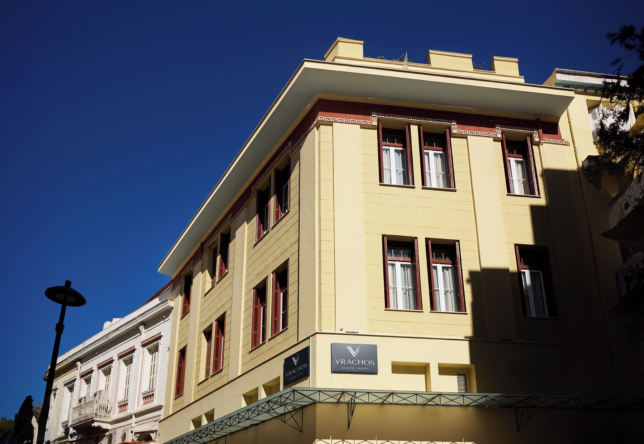 A yellow building with a sign for 'VRACHOS ALTERNATES SUITES'.