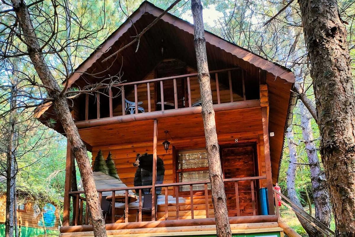 Egy faépítésű ház, verandával, melyet fák öveznek.