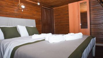 Una cama bien hecha con sábanas blancas y detalles verdes, techo de madera y armario de madera.