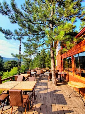An outdoor dining area with wooden tables and chairs, surrounded by pine trees, and overlooking a mountainous landscape. - ÇAMPINARI DOĞA EVLERİ & RESTAURANT (Mengen)
