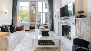 Ein geräumiges Wohnzimmer mit Kamin, Fernseher und einem großen Fenster mit Vorhängen.