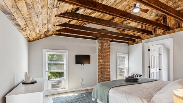 Un dormitorio con techo de madera, un pilar de ladrillo, una cama con manta verde y un televisor de pantalla plana montado en la pared.