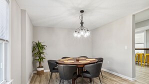 Comedor con una mesa redonda, sillas negras, una planta en maceta y un candelabro moderno.