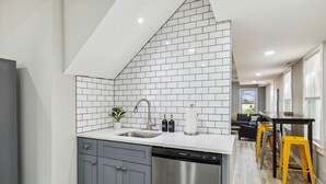 Una cocina moderna con gabinetes grises, lavavajillas de acero inoxidable y salpicadero de azulejos blancos.