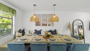 A dining room with a large table set for six, blue chairs, two hanging wicker lamps, and a window with blinds.