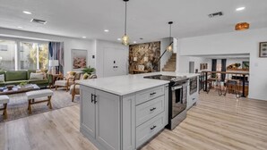 A spacious living area with a large island kitchen, a dining area with bar stools, and a staircase leading to an upper level.