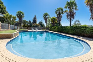 A swimming pool with a curved edge, surrounded by a brick deck and a metal fence.