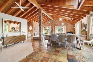 Un'ampia stanza con soffitto alto, travi in legno a vista, un camino in mattoni e un'area pranzo con sedie e tavolo.