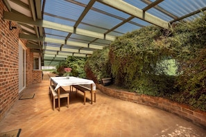 Une serre avec un mur en briques, une table avec des chaises et un feuillage dense.